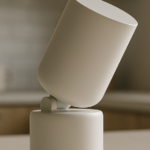 Matte-white screenless cylindrical smart speaker with a tilted mechanical neck on a minimalist kitchen countertop in soft ambient light