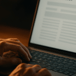 Hands hovering over a laptop keyboard showing a newsletter article with a percentage score overlay, lit by a warm desk lamp